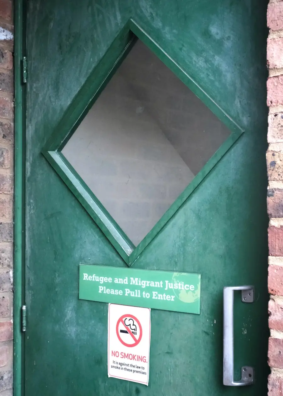 Colour photograph of a green door with a sign on the door reading Refugee and Migrant Justice Please Pull to Enter