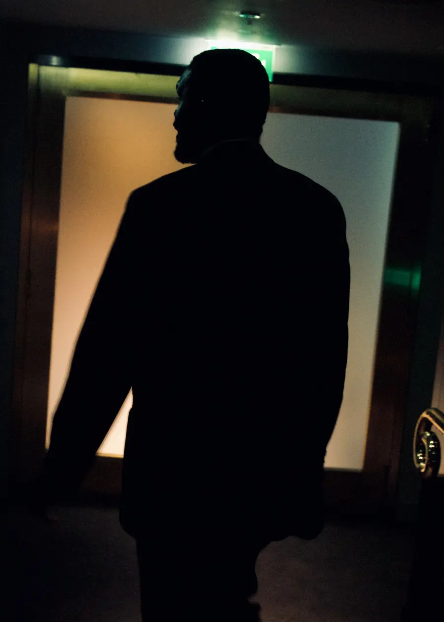 Colour photograph of a man with his back to the camera, silhouetted against a backlit door