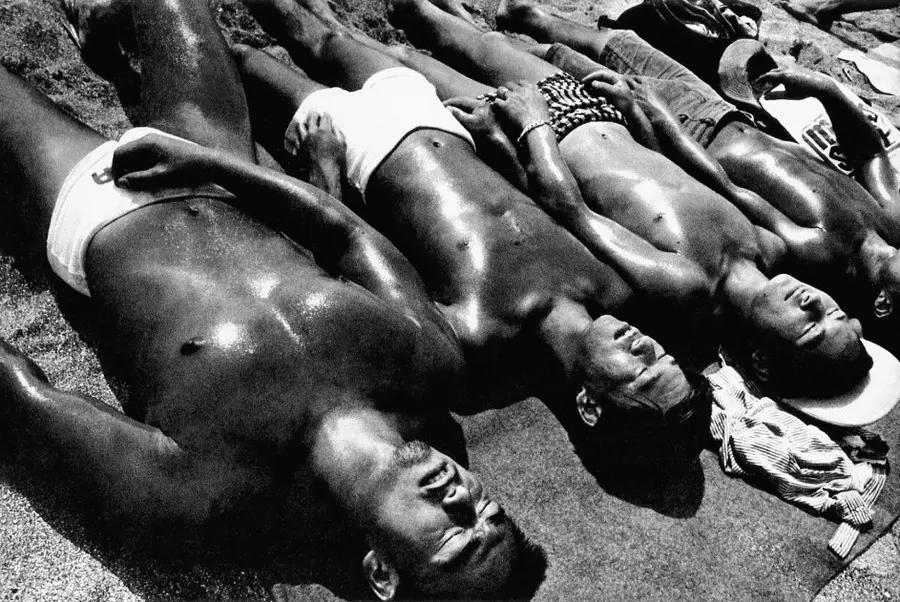 Black and white photograph of a row of shirtless sunbathing men