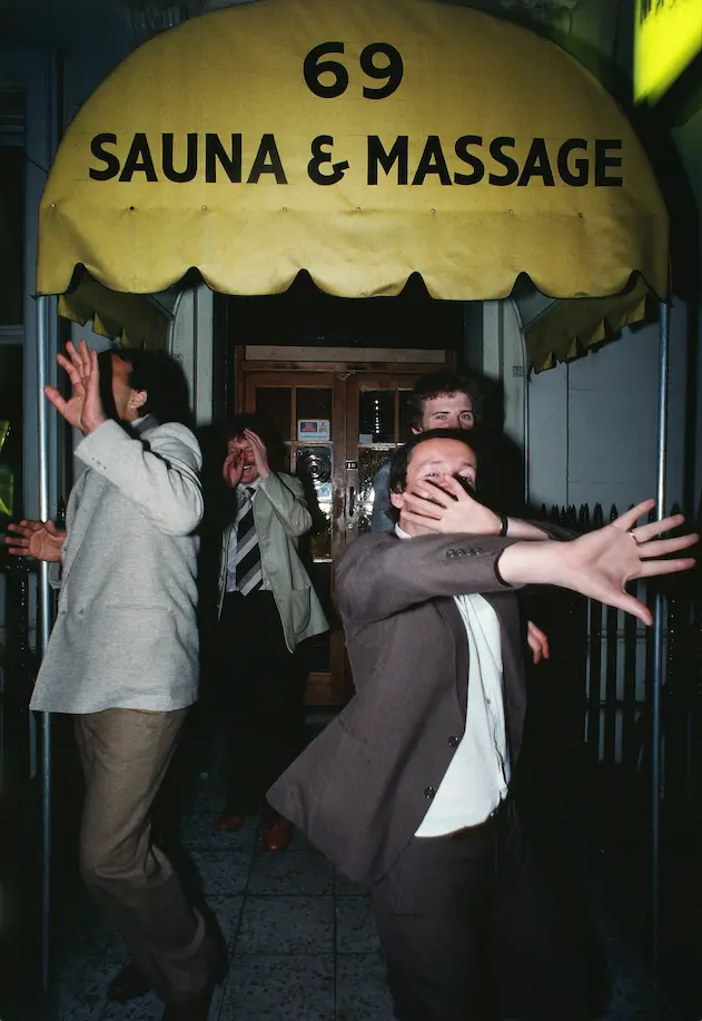 An image of men hiding their faces leaving 69 Sauna & Massage by William Klein