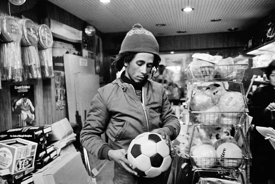 Black and white photograph of a young Bob Marley holding a football in a sports shop.