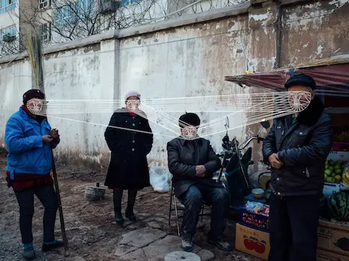 Four figures face the camera in front of a fruit and vegetable stand. Their faces are connected by a web of overlaid white lines. 