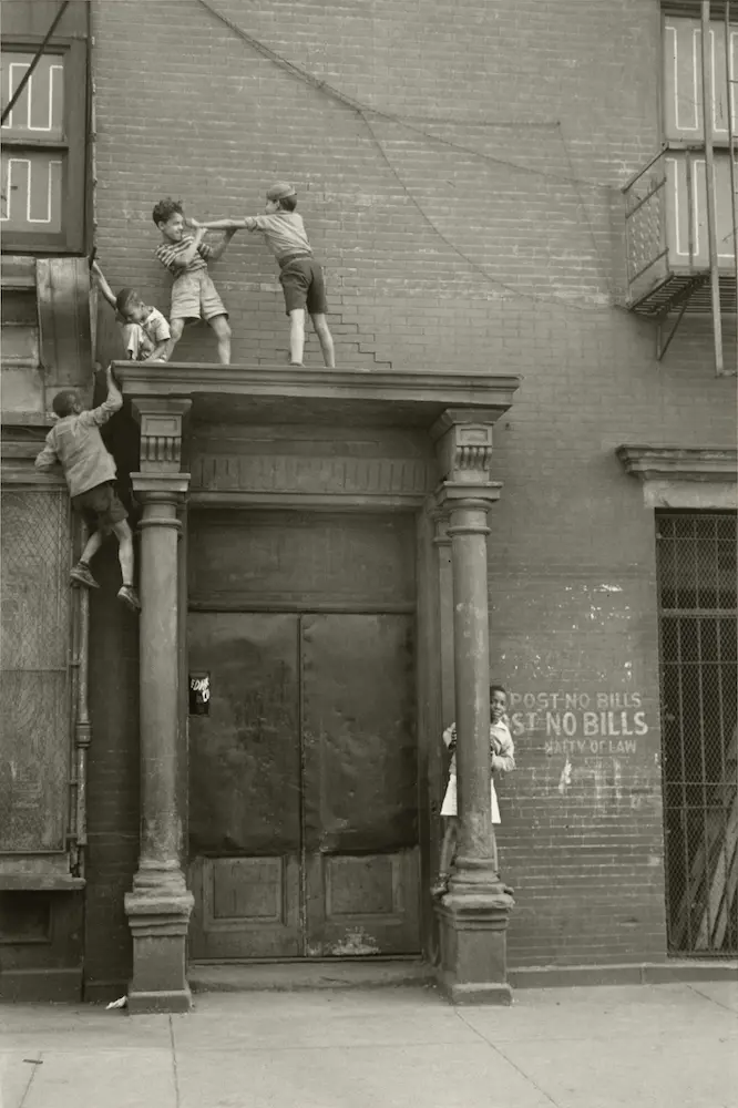 Five boys climb or stand atop the portico entrance of a brick building.