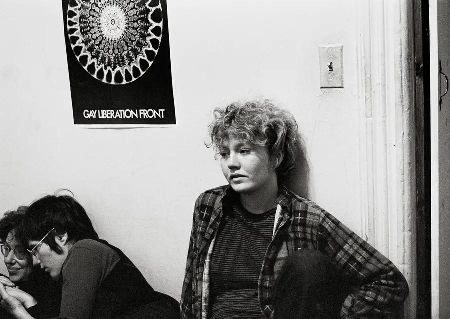 Two young people are sat below a poster that reads "Gay Liberation Front"