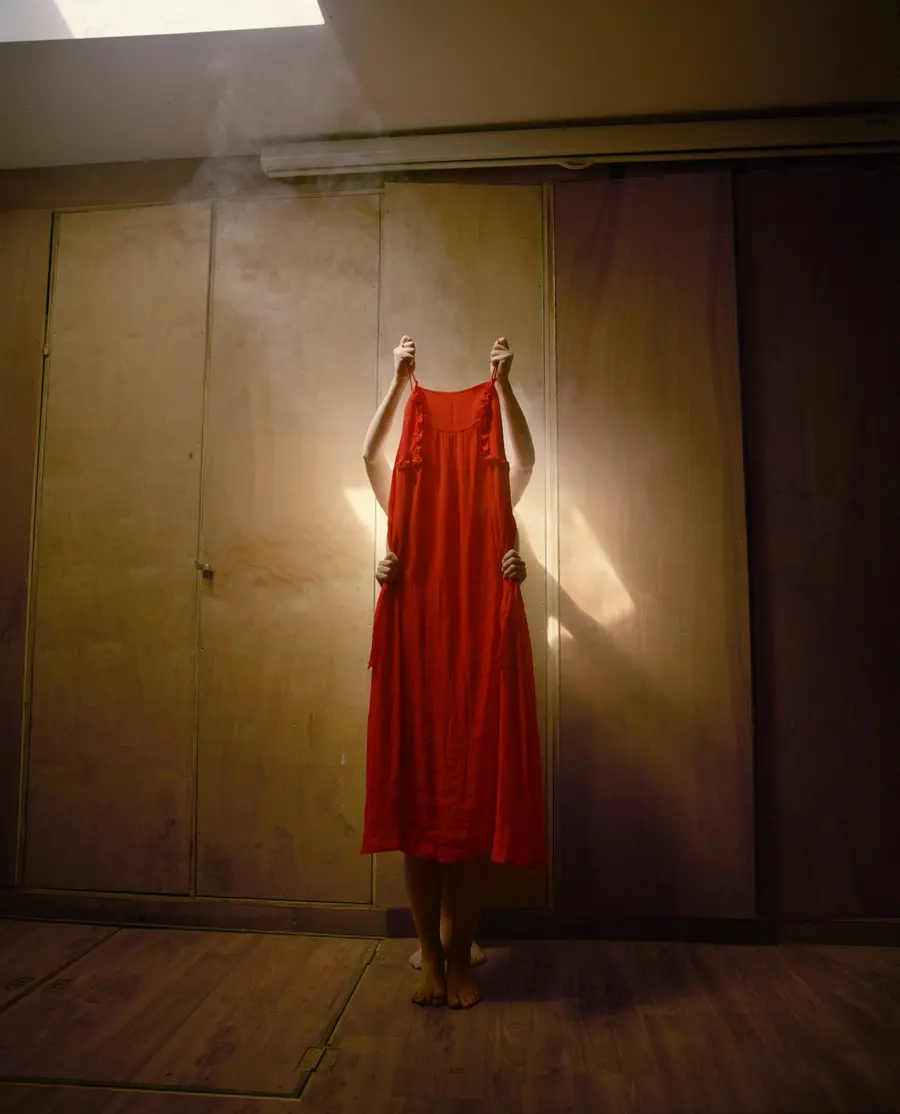 Colour photograph of a two unidentified people holding up a red dress.