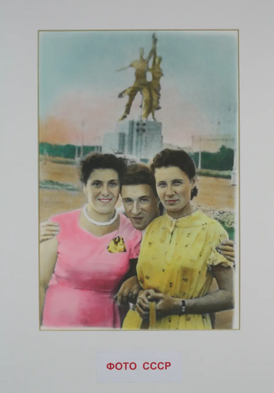  Colour photograph of three women posing  with a monument featured in the background. Two of the  women can be seen in a pink dress and a yellow dress. 