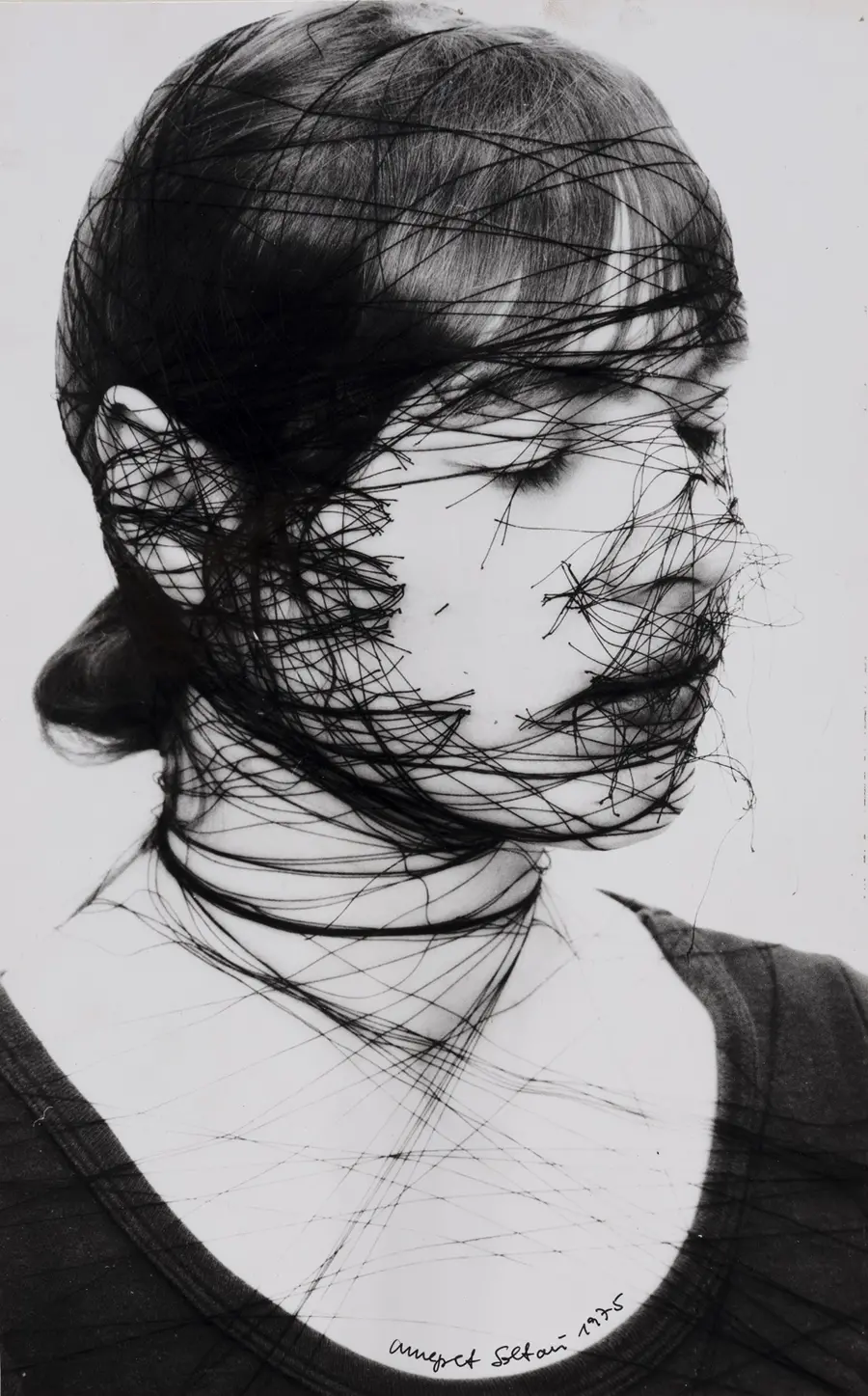 Portrait photograph of a woman with black string wound tightly around her head that has been cut apart.