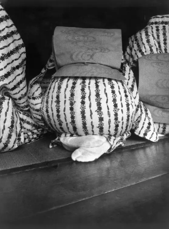 Black and white photograph of the back of a kneeling and bowing  woman in traditional Japanese clothing.