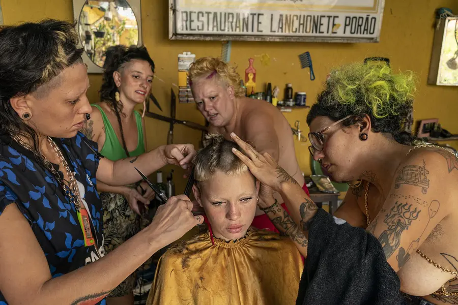 Four women with partially shaved and colourful hair attend to cutting a styling the hair of a younger woman.
