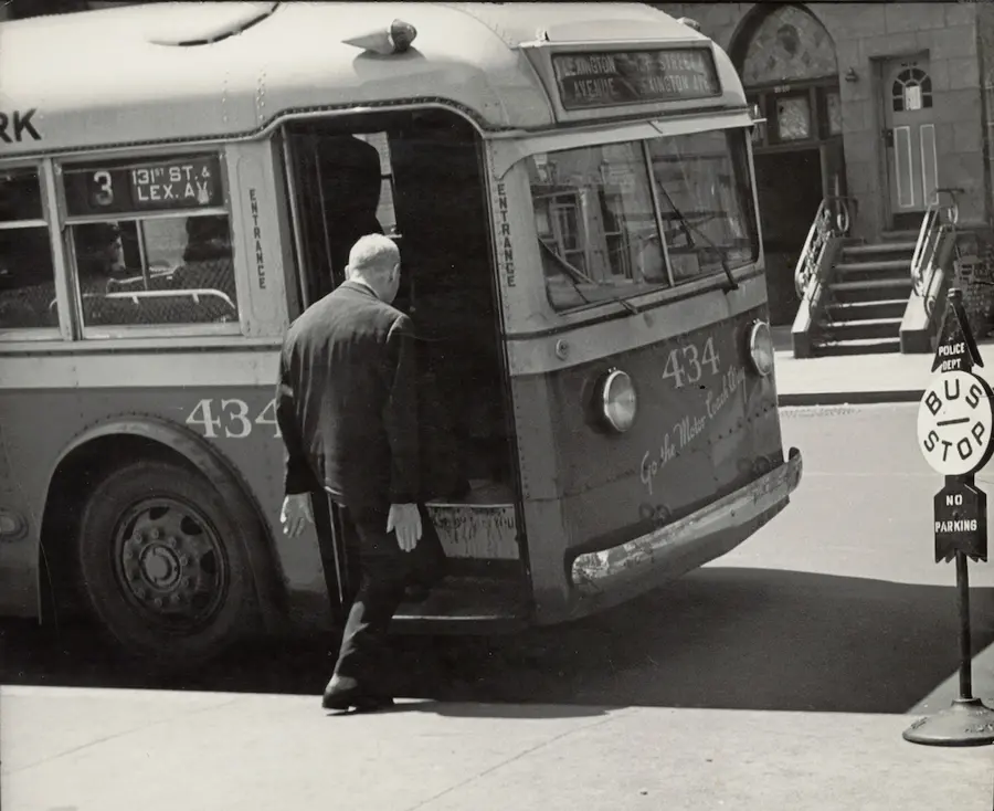 An older man boards a bus, hands at his side looking forward.