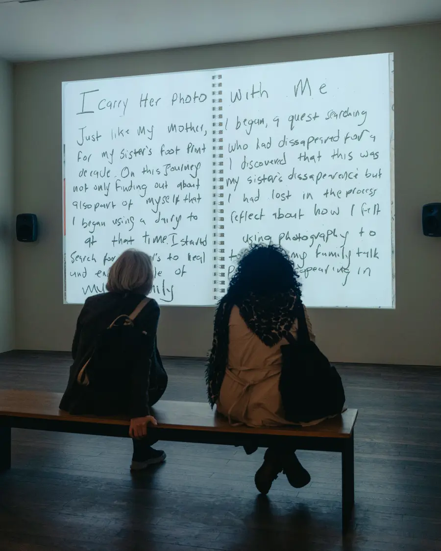 Colour image of two people sat watching an image projected onto a gallery wall.