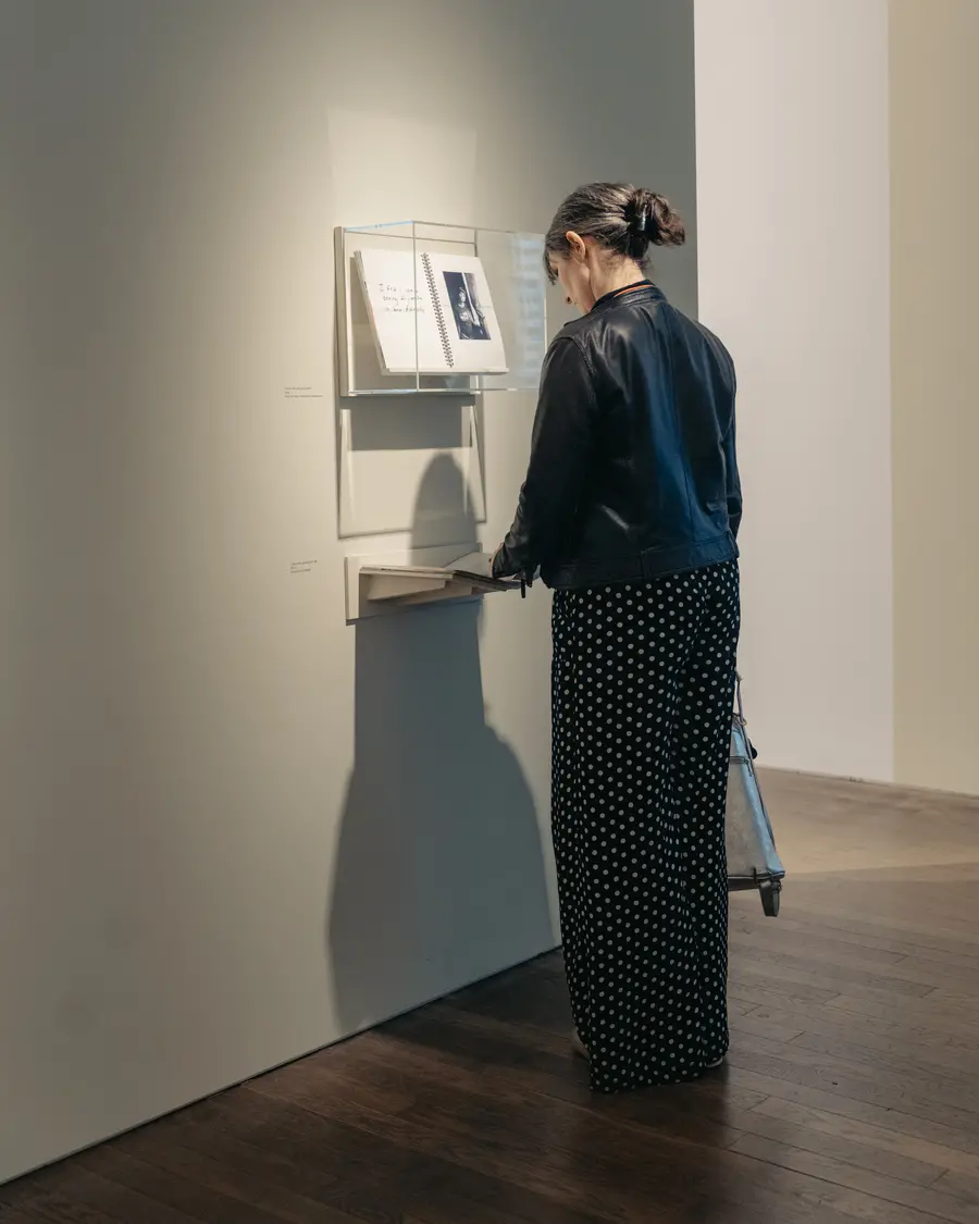 Colour image of a person flicking through a book that is on display in an exhibition space.