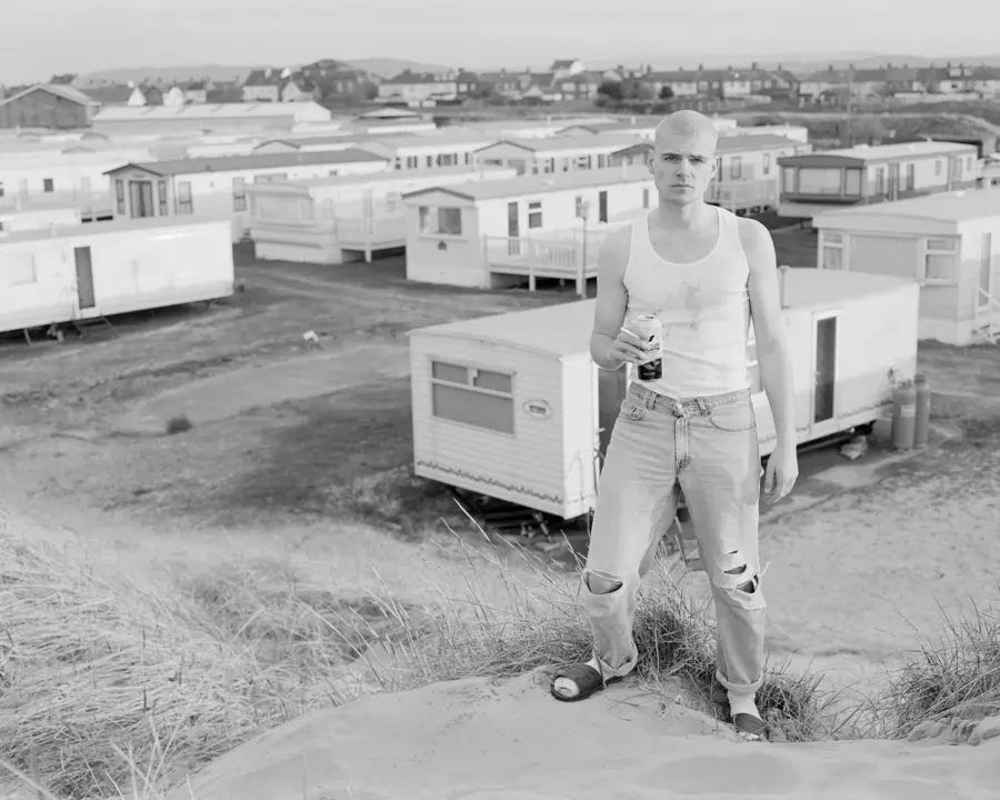 A person stands in the foreground with a motorhome site in the background.