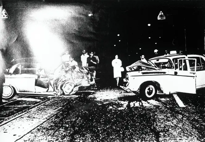 High contrast black and white photograph of two severely damaged cars and a small crowd