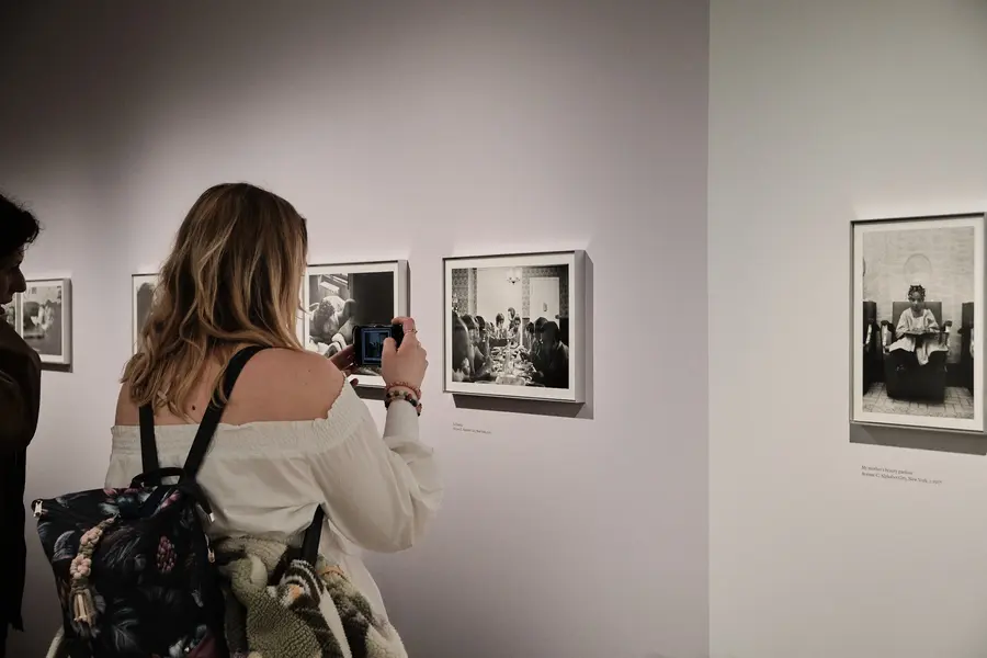 A young woman taking a photo with her phone of a framed picture in an exhibition.