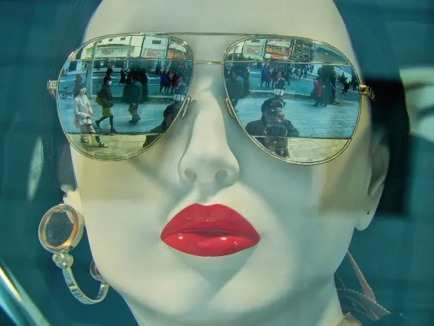 Colour photograph of a mannequin head with red lipstick, wearing sunglasses which reflect a street scene