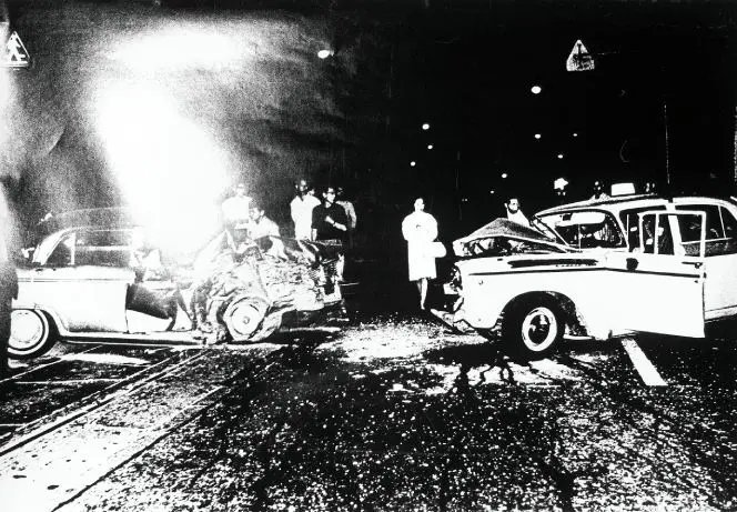 High contrast black and white photograph of two severely damaged cars and a small crowd gathered