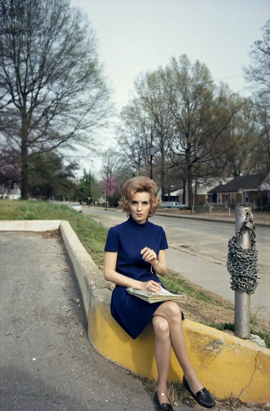 Colour photograph of a woman sitting on the edge of the yellow kerb.