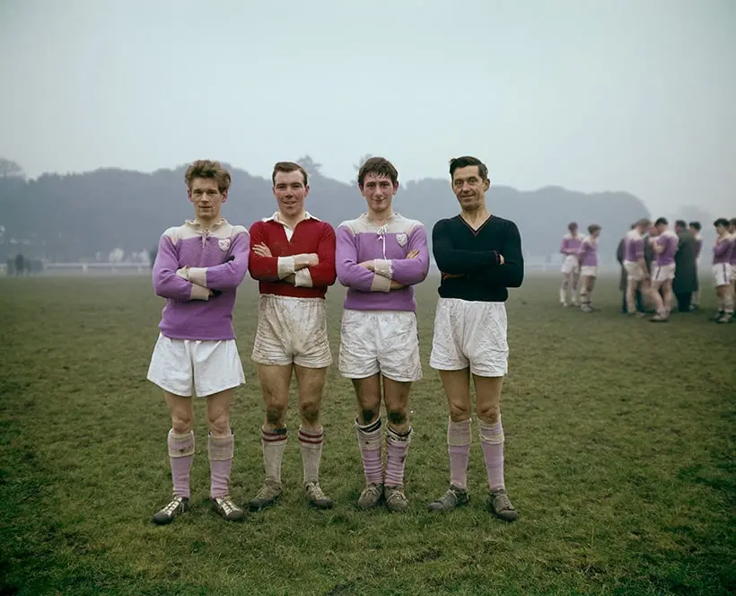 Four men stood in a row in a football field dressed in 1960s football kits