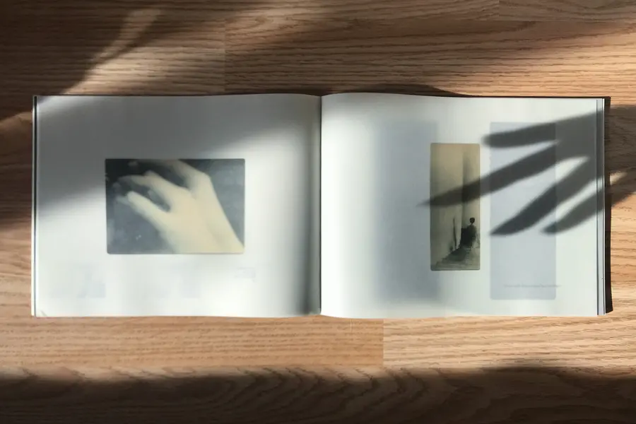A photograph of a book laid out on a table with shadows of hands going across the page.