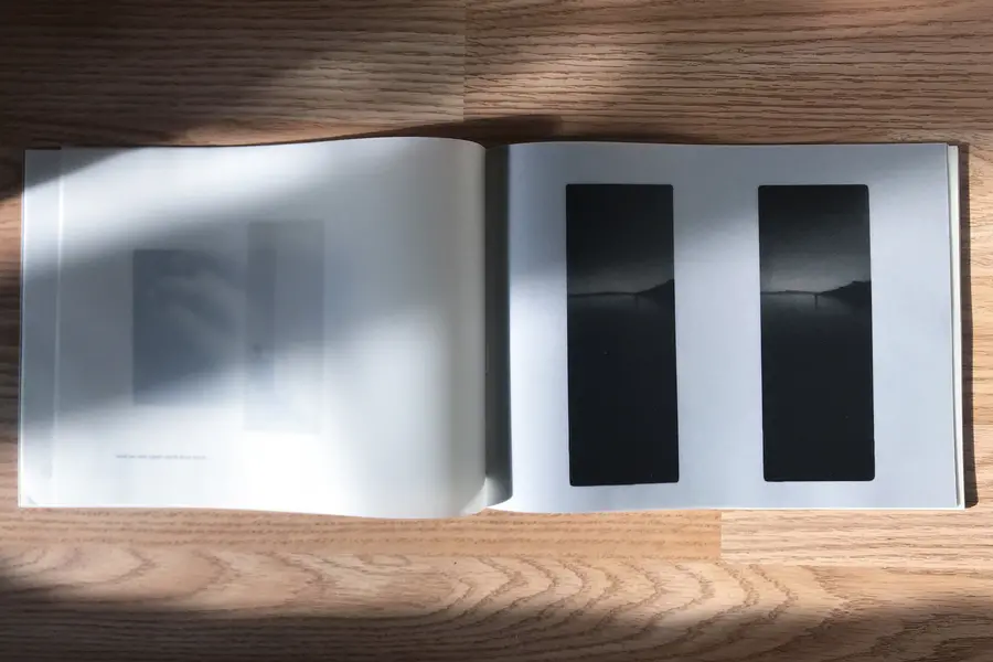 A photograph of a book laid out on a table with shadows of hands going across the page.