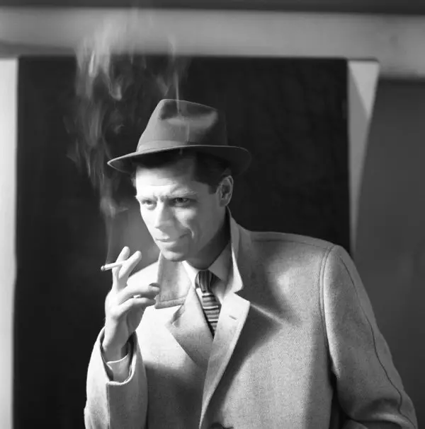 Black and white photo of a male model posing while smoking a cigarette.