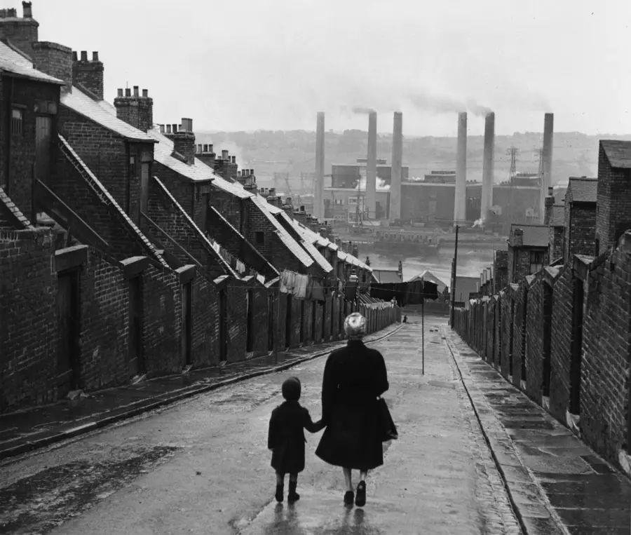 Black and white photo of a woman and child walking down a residential street.