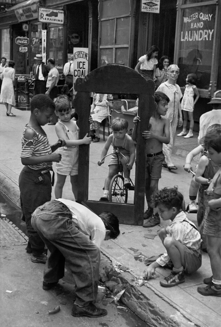 A group of children stand on a street holding a large frame for a mirror with shattered glass below