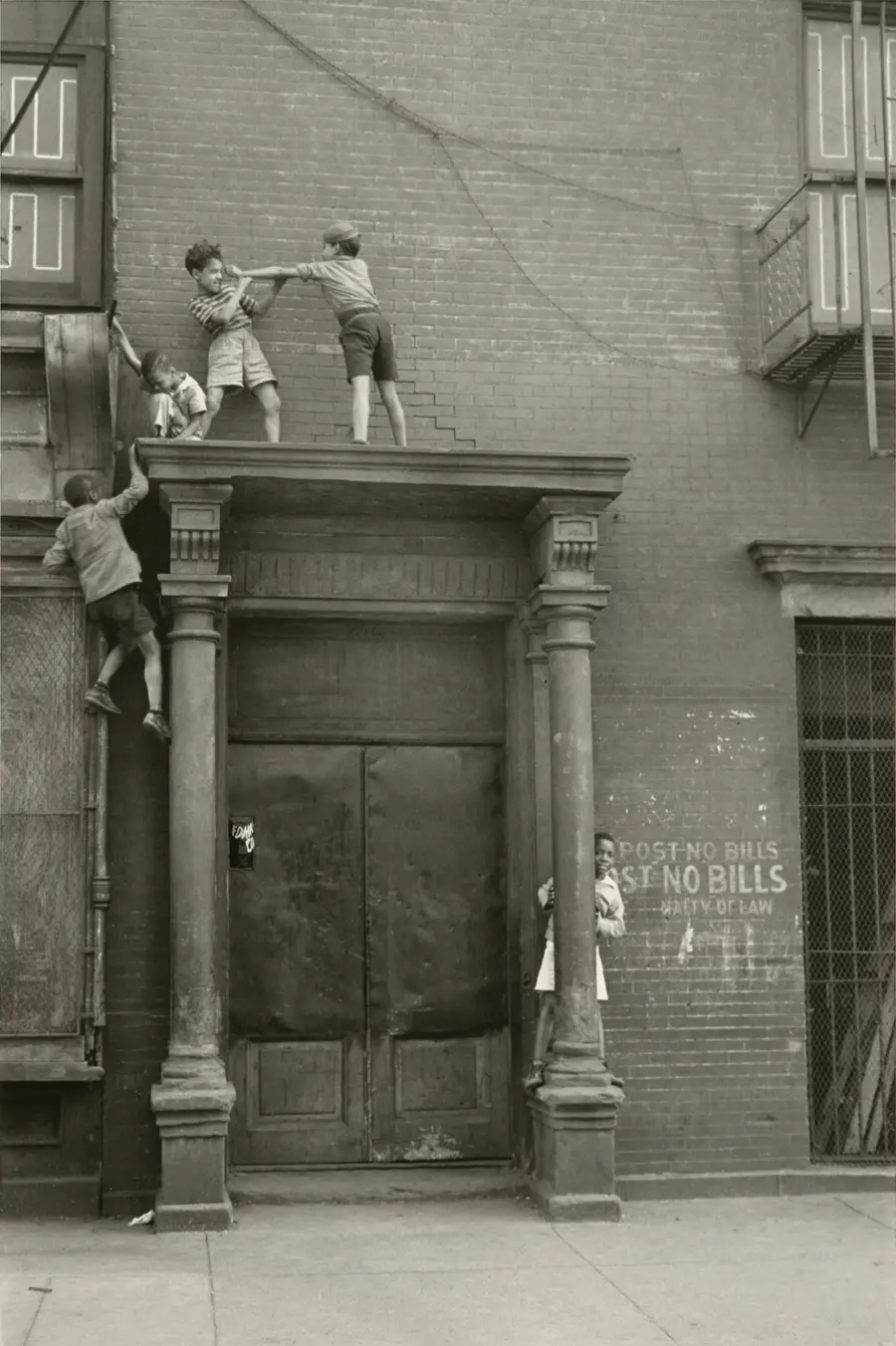 Five children climb and play on the portico of a doorway on the street