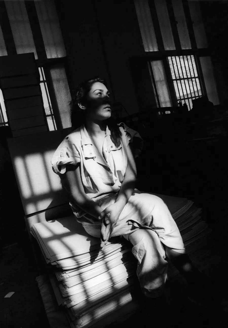 Black and white photograph of a woman sat on a prison bed staring into the distance.