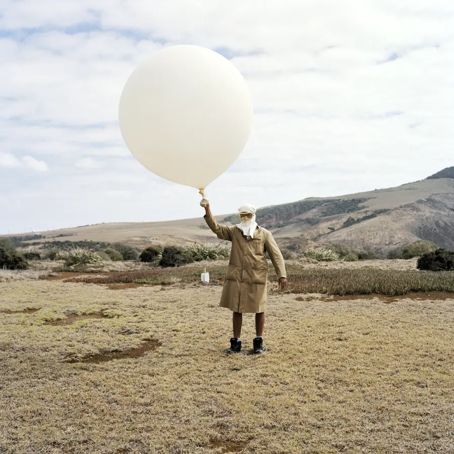 A person is standing in the middle of a landscape, holding up a white baloon