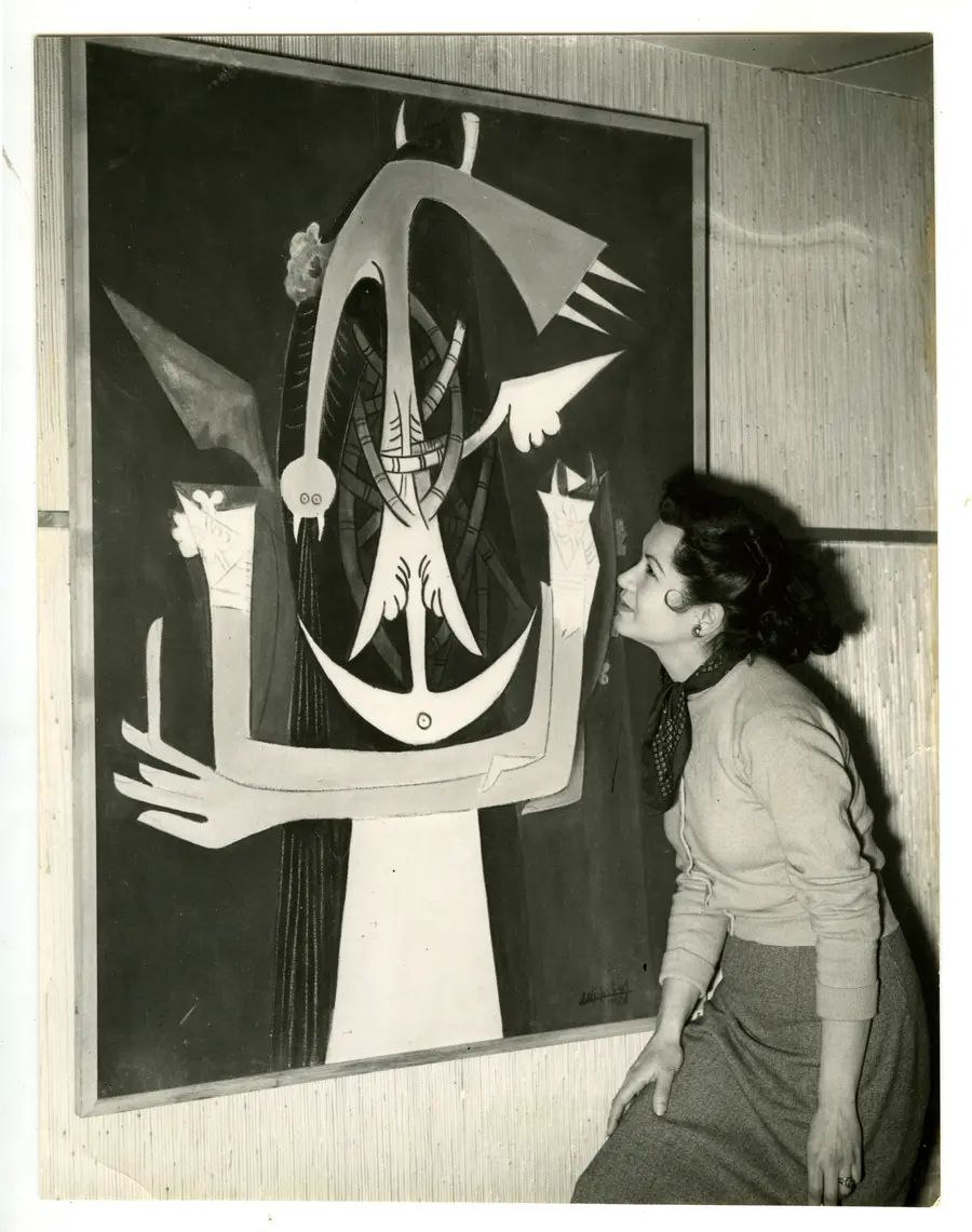 A black and white image of a woman in profile looking closely at a large modernist painting