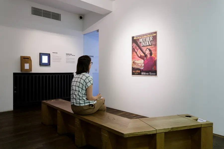 Person sitting on a bench in front of a 1970s poster featuring a woman in a sari with a yoke over her shoulder.