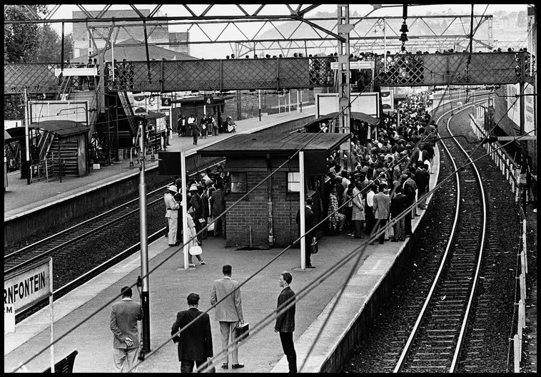 Black and white photograph of a segregated railway platform. On one end the platform is packed with black passengers and the other end has only a few white passengers waiting
