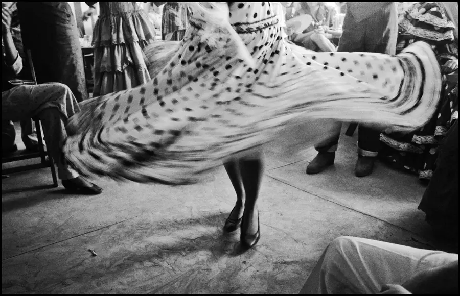 Black and White photograph of a woman, wearing a long skirt and dancing in the middle of a room