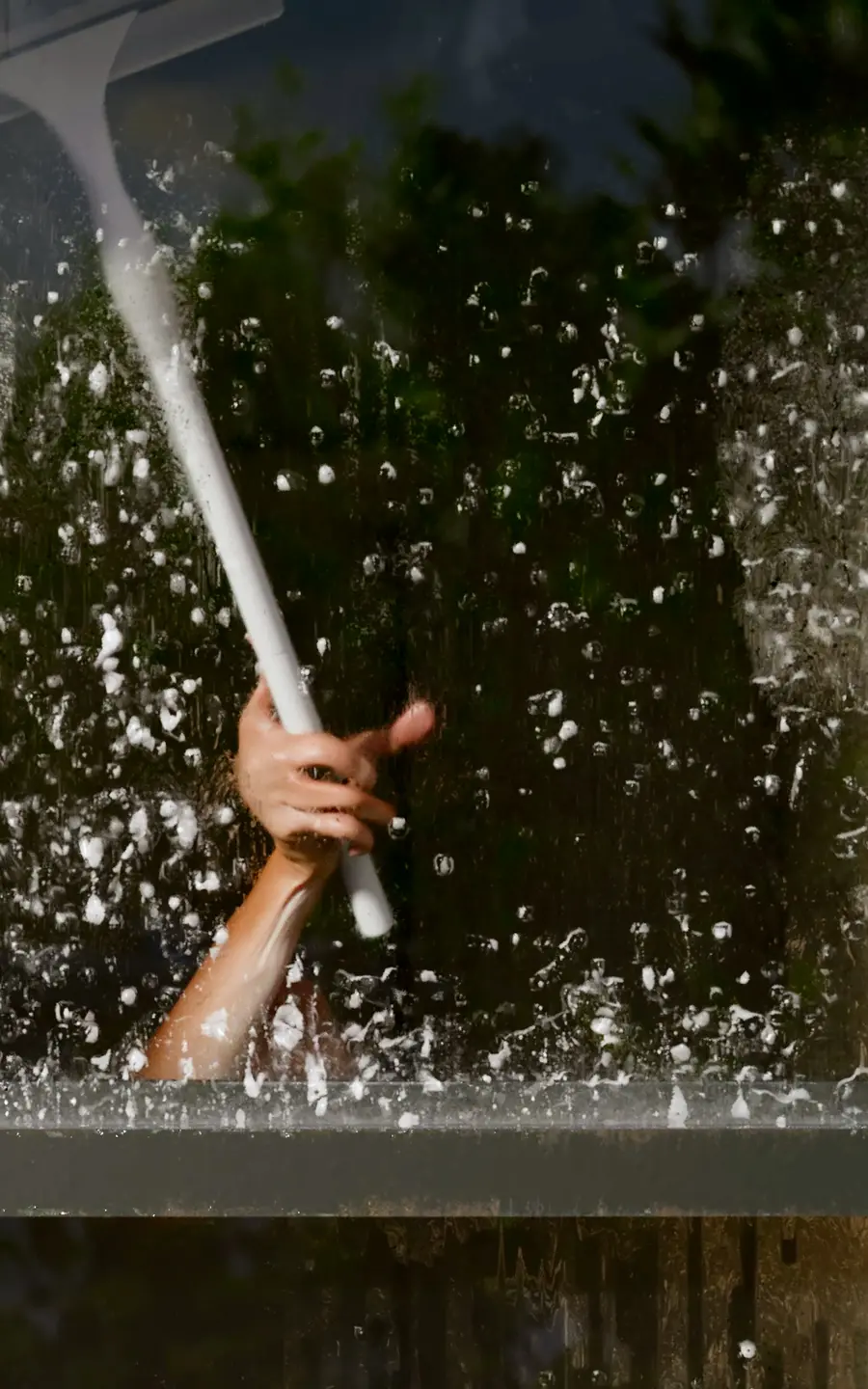 A 3D animated hand washes a soapy window with a squeegee 