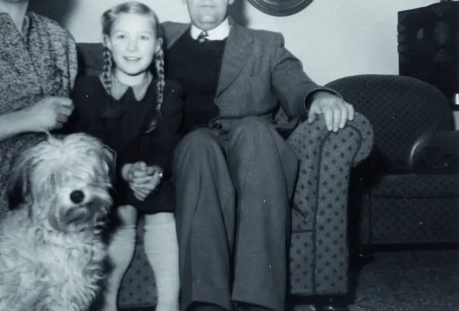 Black and white photograph of a family sitting on a sofa. Only the faces of the young girl and dog can be seen in the photo.