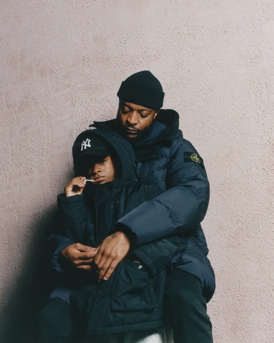 Colour photograph of a young person and adult standing against a wall