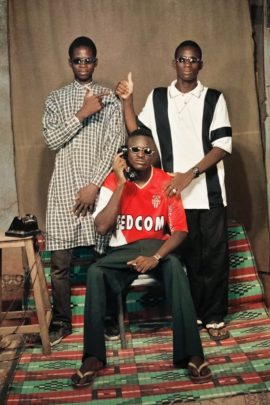 Colour photograph of three young men posing for the photograph, one is seated on a chair whilst the other two are stood behind him.