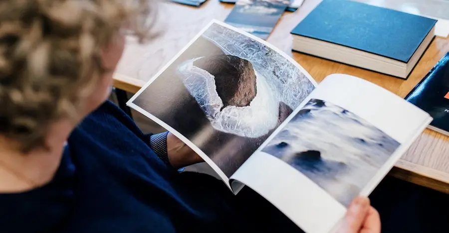 A person with curly hair looking at a photobook that shows an image of the ocean.