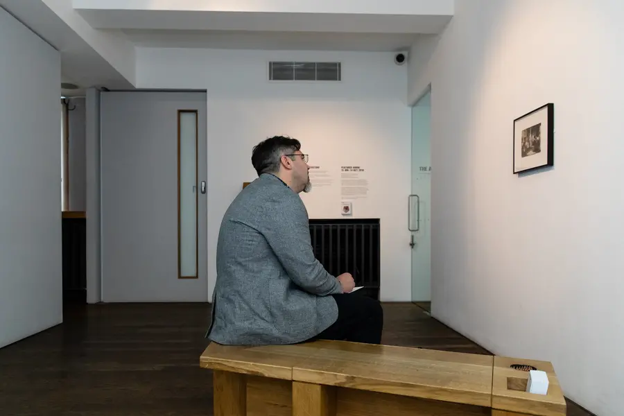 A man seated on a bench looking at a framed, black and white photograph.