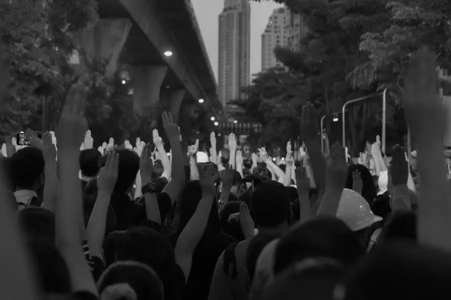 A black and white photograph of a crowd holding their hands up in the street.