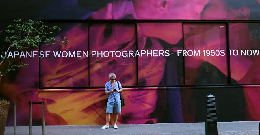 Image of The Photographers Gallery with a colourful image wrapped across the windows. A man is stood casually in front of the building checking his phone.