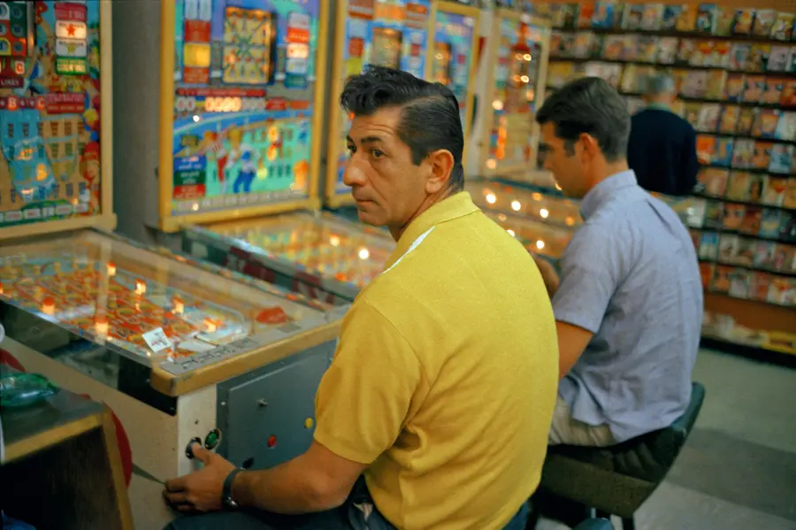 Colour photograph of two men sat in front of pinball machines.