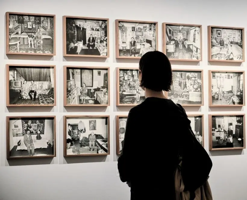 A woman looks at a series of framed black and white photographs displayed on a white wall.