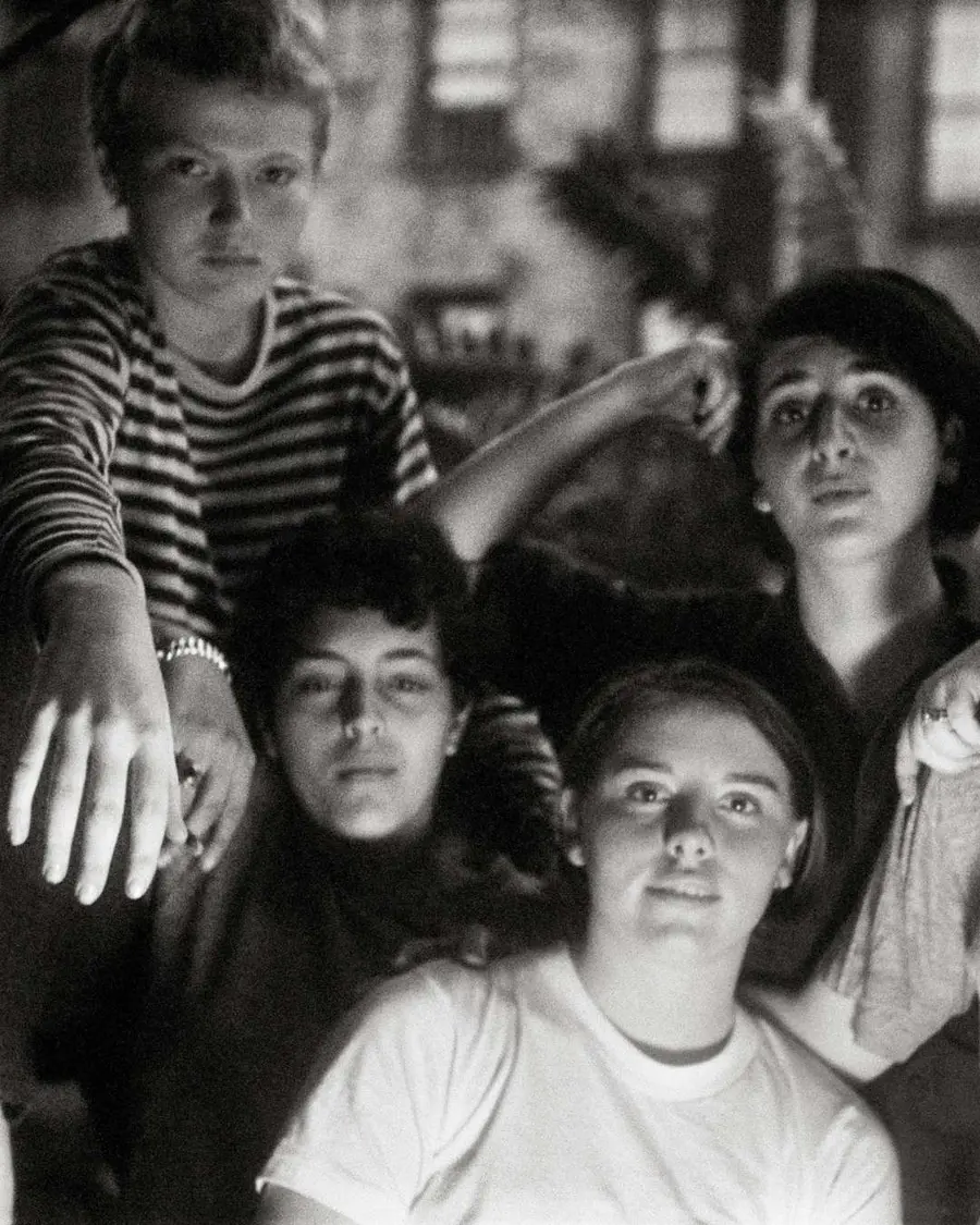 A black and white photo of a group of young queer women sat together looking toward the camera.
