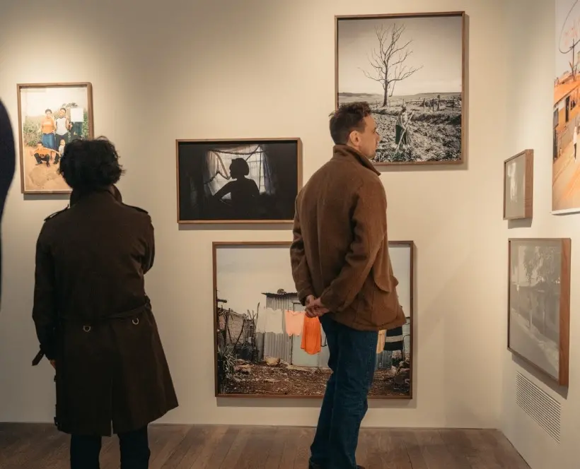 Colour image of two people looking at photographic prints displayed on a gallery wall.