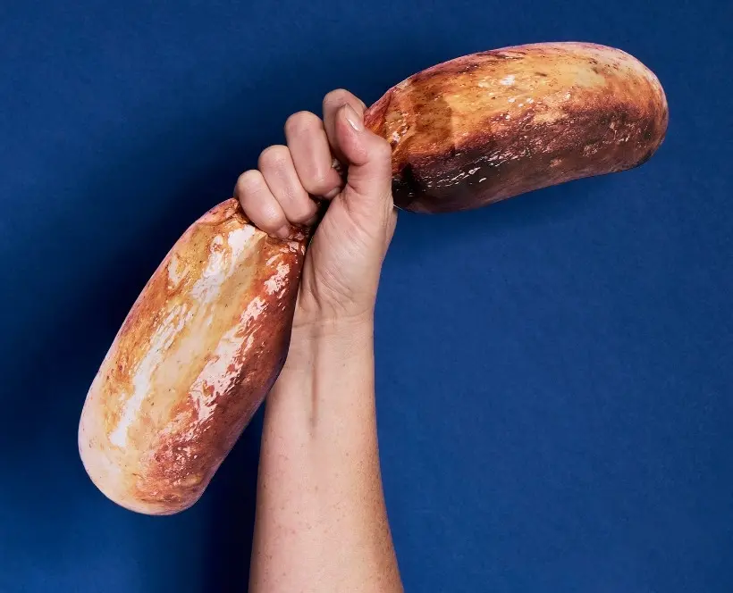 A photograph of a hand holding a large sausage against a blue background.