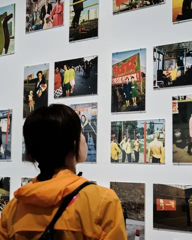 Colour photo of a person wearing an orange raincoat looking at works in the exhibition space.