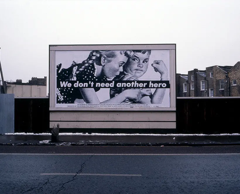 Black and white photograph of a billboard featuring a vintage-style advert of two children and the words "we don't need another hero" printed across